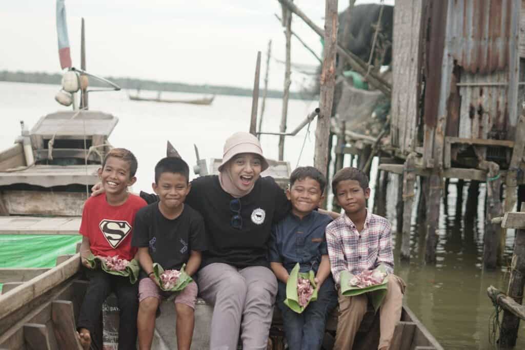 Ditemani oleh anak-anak desa, Chiki mengantarkan daging-daging kurban ke rumah-rumah warga Desa Jaring Halus menggunakan perahu kayu.