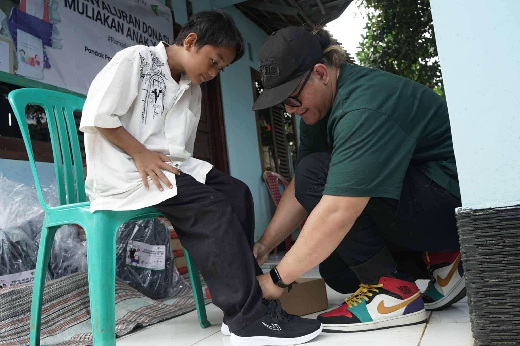 Drummer J-Rocks, Anton Rudi Kelces memakaikan sepatu kepada salah satu anak yatim sebagai bagian dari kado untuk yatim yang diberikan bandnya, Bajawa, dan Dompet Dhuafa.