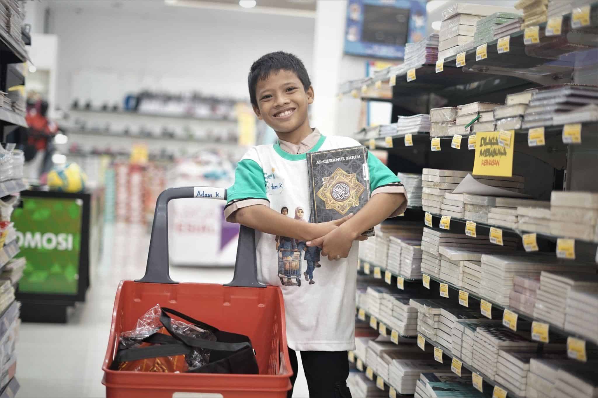 Adam sedang tersenyum lebar karena ia bisa memberi Al-Qur'an impiannya melalui Program Belanja Bareng Yatim yang diselenggarakan oleh BSI dan Dompet Dhuafa.