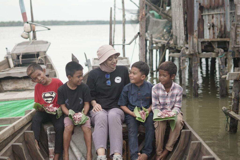 Chiki Fawzi (tengah) mendistribusikan daging kurban ke rumah-rumah warga Desa Jaring Halus, Sumatra Utara menggunakan perahu kayu bersama anak-anak Desa Jaring Halus.